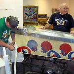 Volunteers remove legs from a pinball game at the National Pinball Museum.